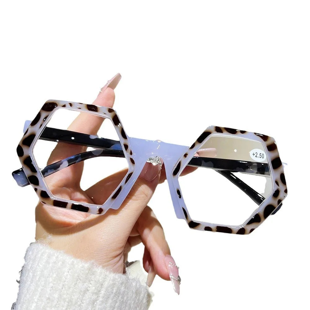 Hexagonal eyeglasses with tortoiseshell frame held by a hand on a white background