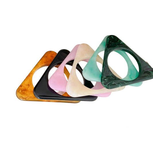 Four triangular acrylic drink coasters with circular cutouts, stacked in a fan arrangement on a white surface. The coasters come in translucent amber, black, pale pink, cream, mint green, and dark forest green marbled finishes.