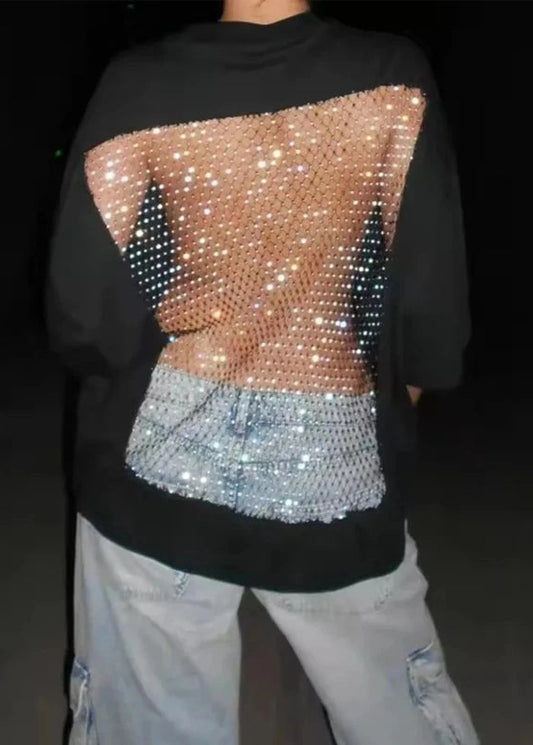 A person shown from the back wearing a black long-sleeve top with a large sequined back panel in rose gold and silver, paired with light gray jeans.